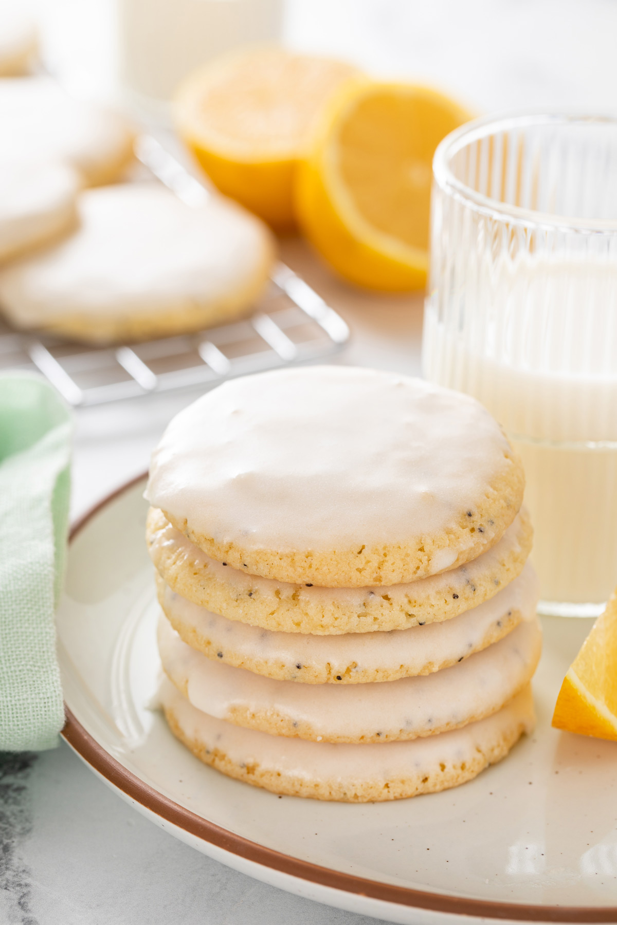 Five lemon poppy seed cookies stacked next to a glass of milk on a plate.